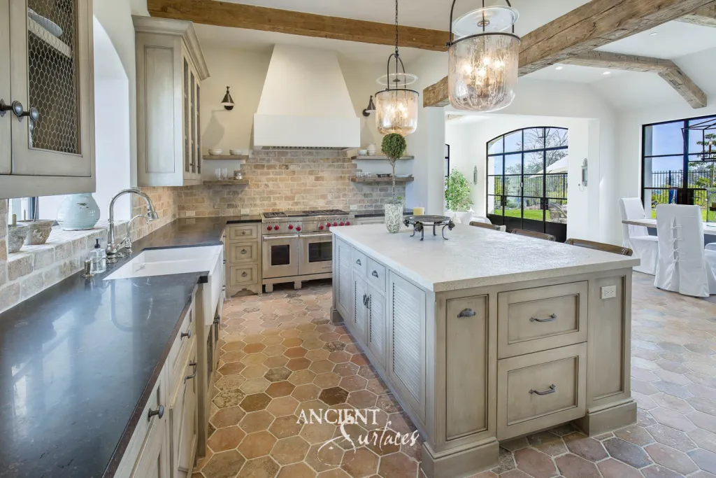 Hexagonal terracotta kitchen floor beneath a reclaimed brick backsplash and a honed natural stone countertop