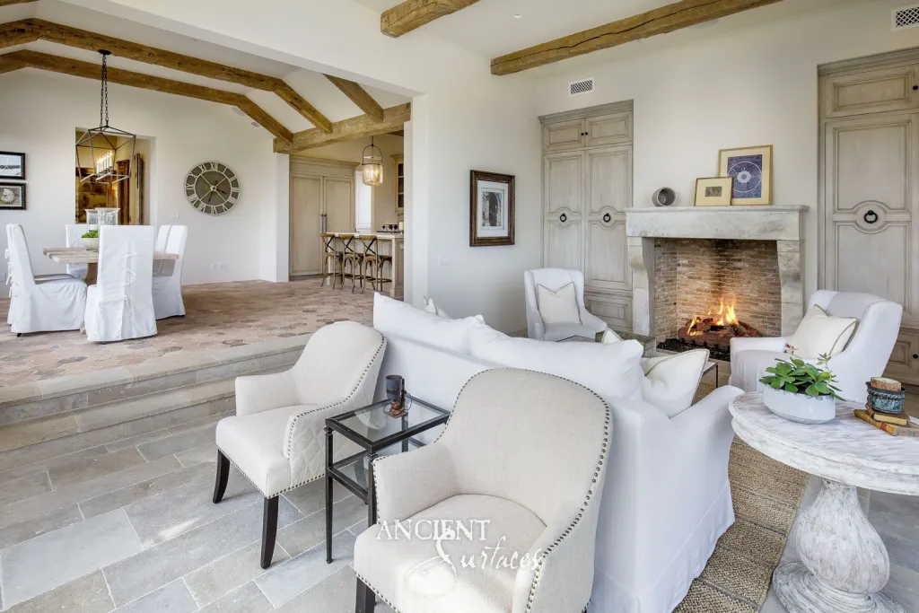 Antique limestone mantel above a herringbone firebrick firebox, with a reclaimed stone floor stepping down from the dining room