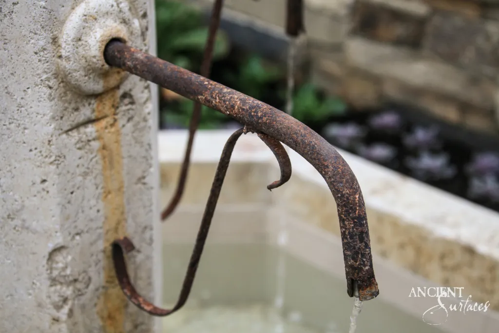 Forged iron fountain spout running water into an antique limestone basin
