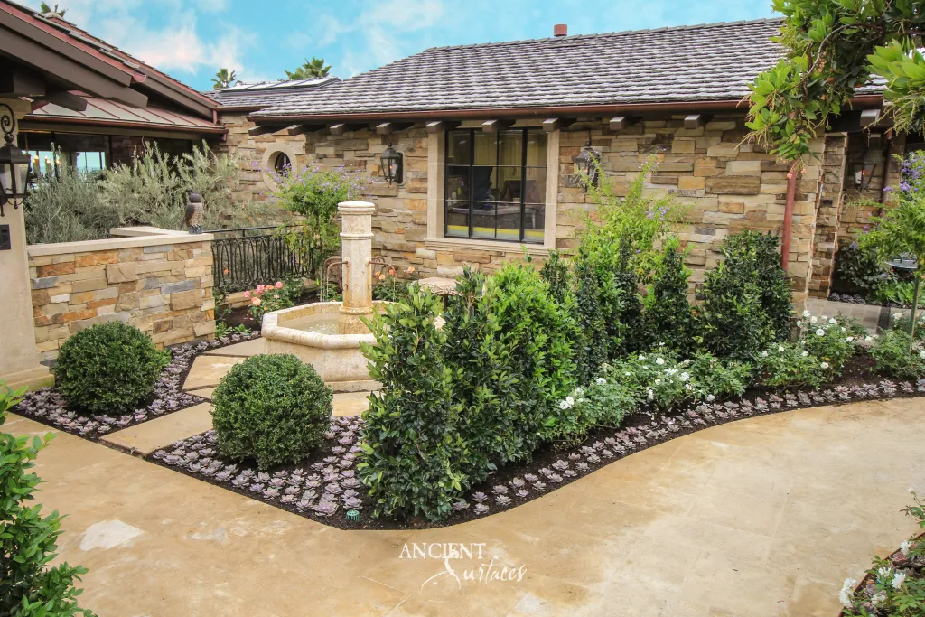 Reclaimed stone paths and terrace paving winding past an antique limestone column fountain in a garden