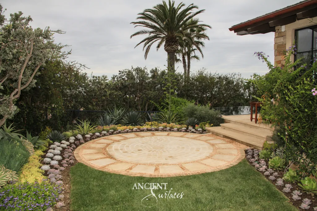 Circular paving medallion of radiating antique limestone wedges inlaid with pebbles, set flush into a garden lawn