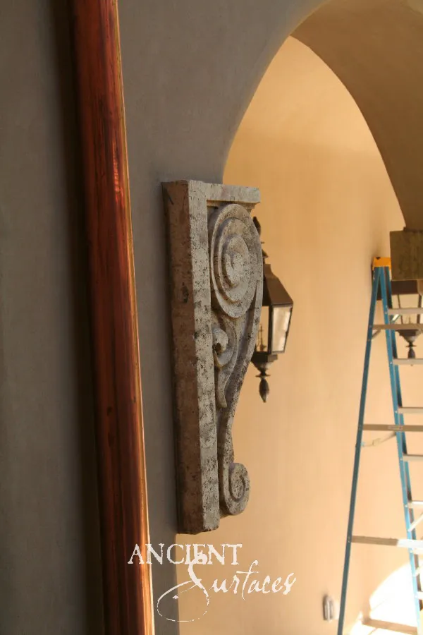 Single antique limestone corbel carved with a volute, mounted on a villa wall beside an arched passage