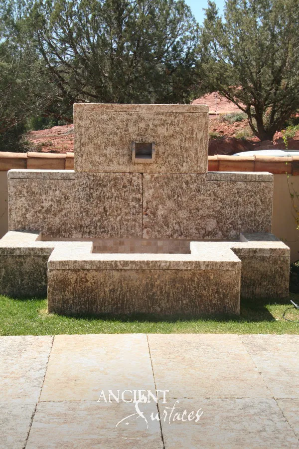 Low reclaimed limestone wall fountain set between two solid stone benches on a paved garden terrace