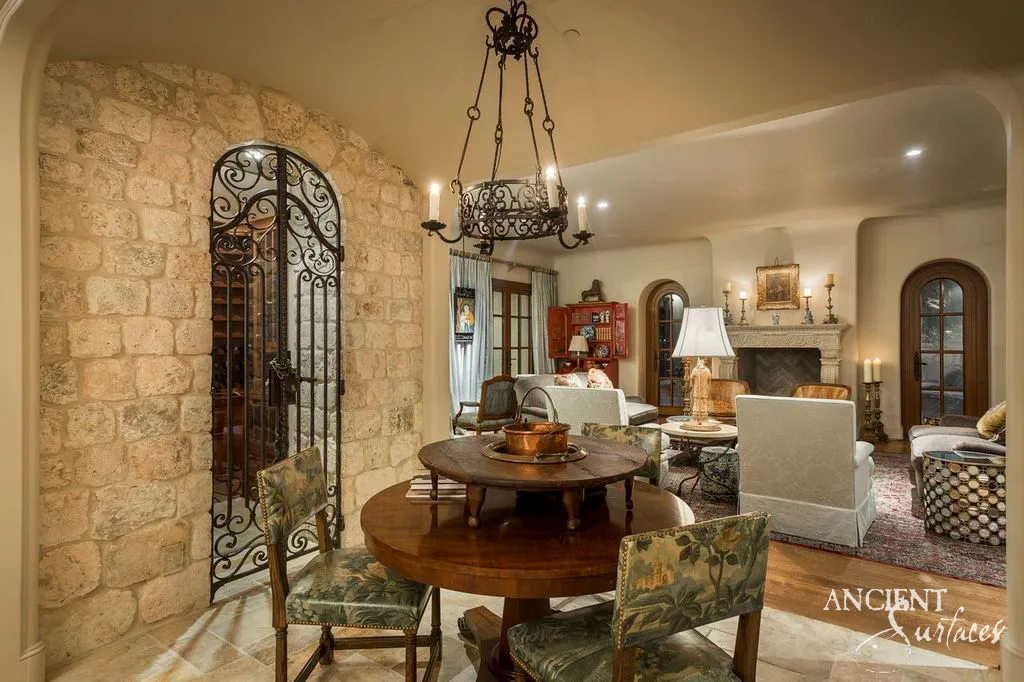 Antique limestone block wall cladding framing an iron wine cellar gate above a reclaimed stone tile floor