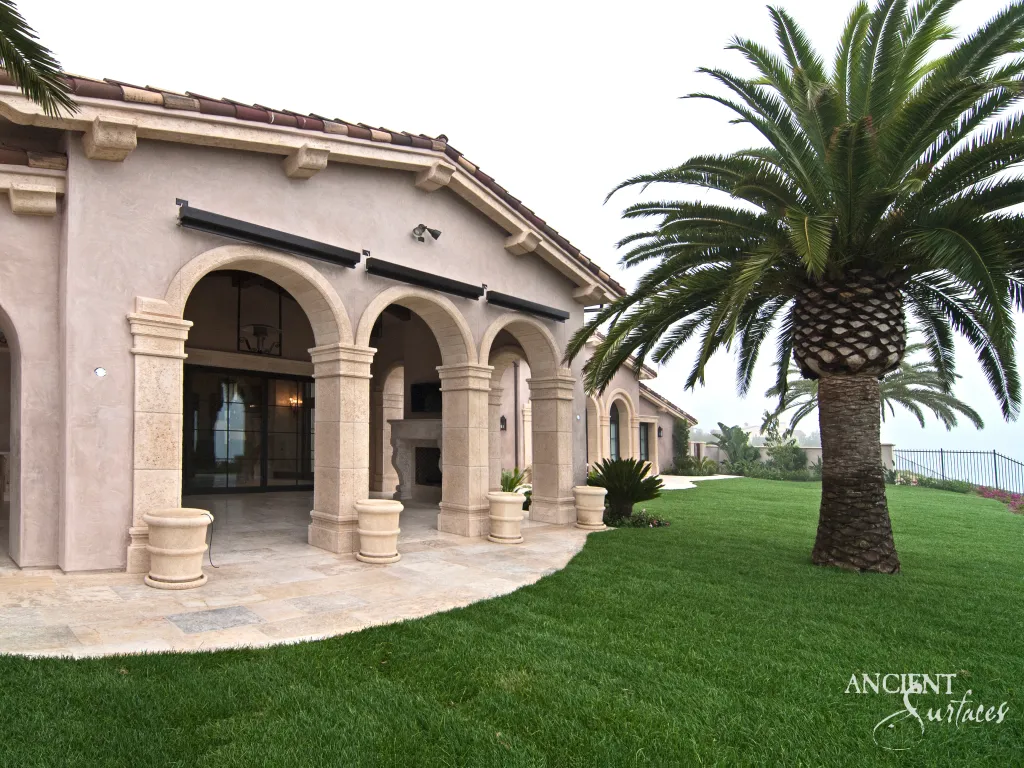 Reclaimed limestone columns and arches framing the loggia of an estate above a stone paved terrace