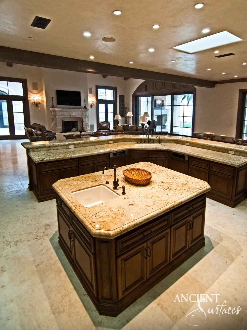 Estate kitchen with polished stone countertops on a limestone floor, opening to a carved limestone mantel beyond